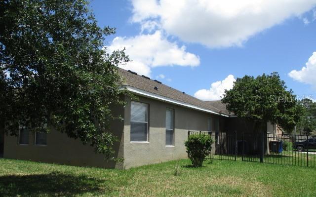 The exterior of a tan stucco house with a dark shingled roof and metal fence — 3827 SPIRITED CIRCLE, ST CLOUD, FL