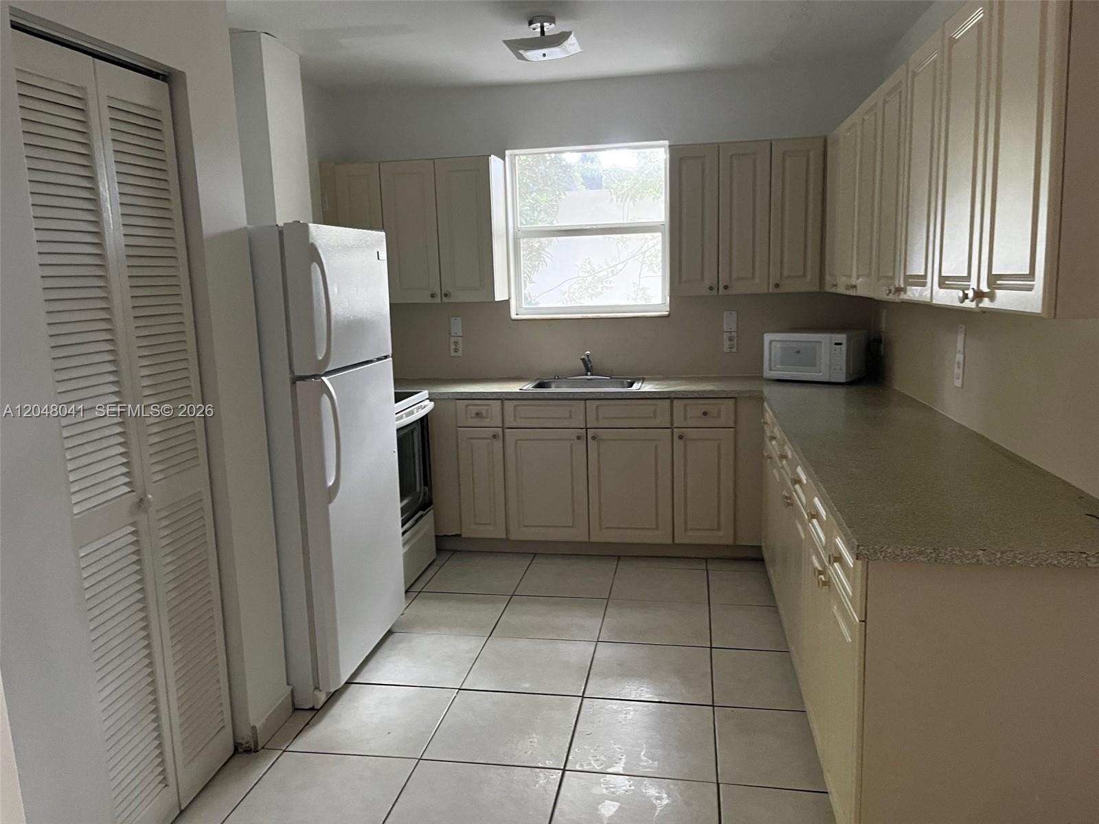 A kitchen features light-colored cabinets, a white refrigerator, a window, and tiled flooring — 181 NW 47th Ave # 25, Miami FL 33126, MIAMI, FL