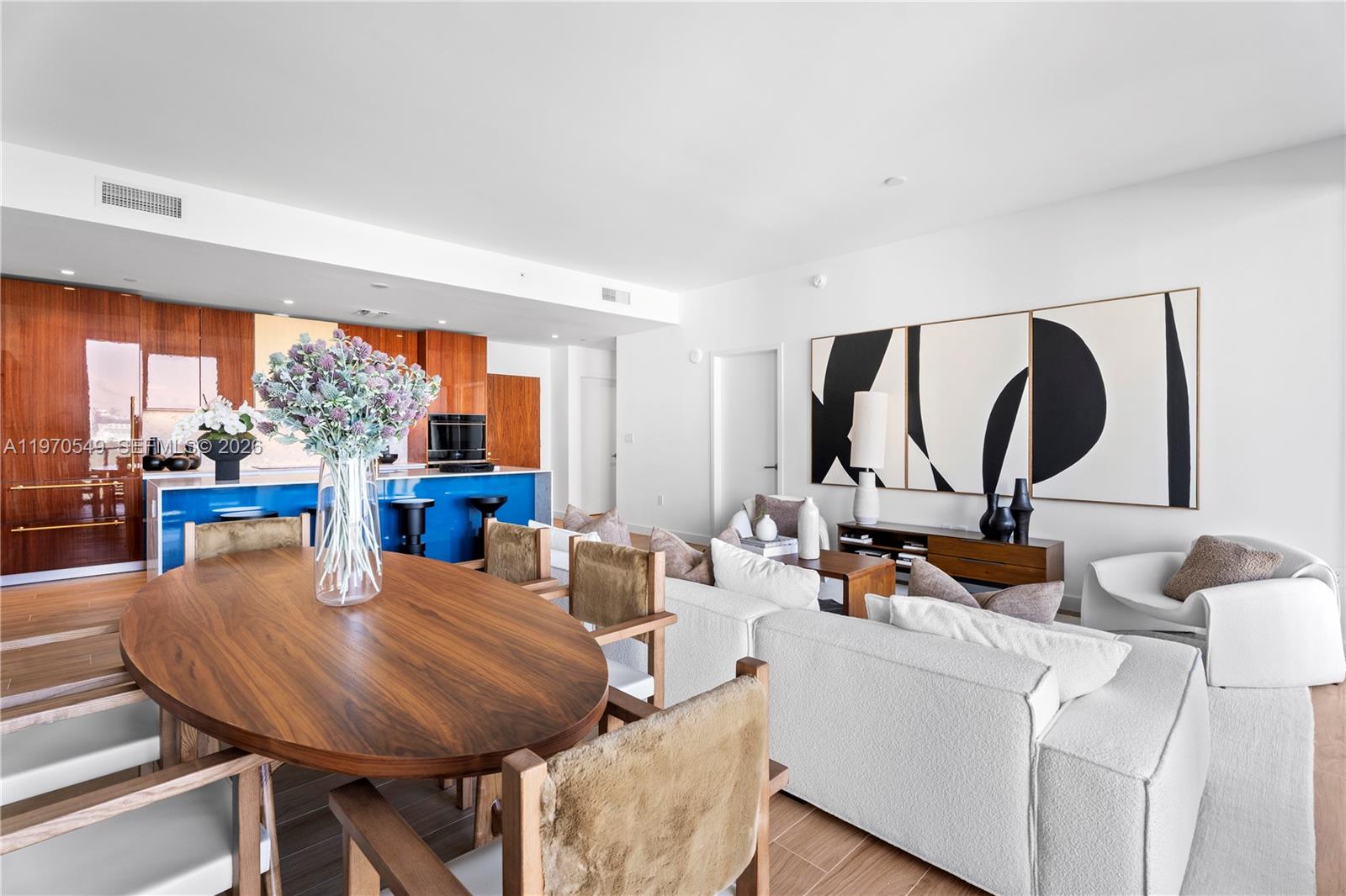 An open-concept living and dining area features wood cabinetry, a blue island, and modern furniture — 2678 Tigertail Ave # 1202, Miami FL 33133, MIAMI, FL