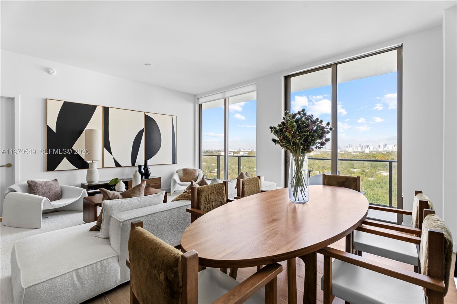 A modern dining and living area features an oval wood table and floor-to-ceiling windows — 2678 Tigertail Ave # 1202, Miami FL 33133, MIAMI, FL