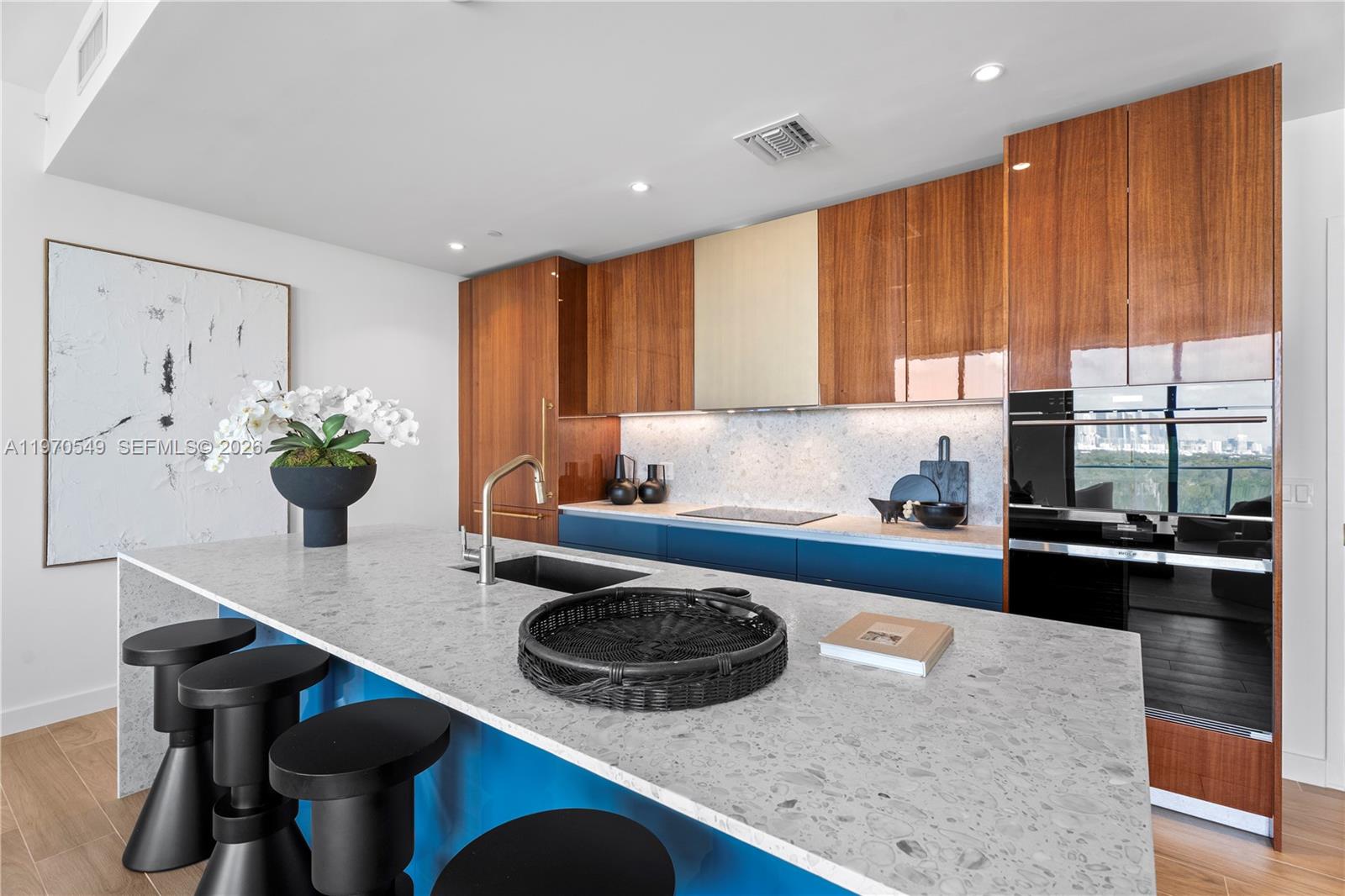 A modern kitchen features a large speckled island, blue cabinetry, and wood-paneled upper cabinets — 2678 Tigertail Ave # 1202, Miami FL 33133, MIAMI, FL
