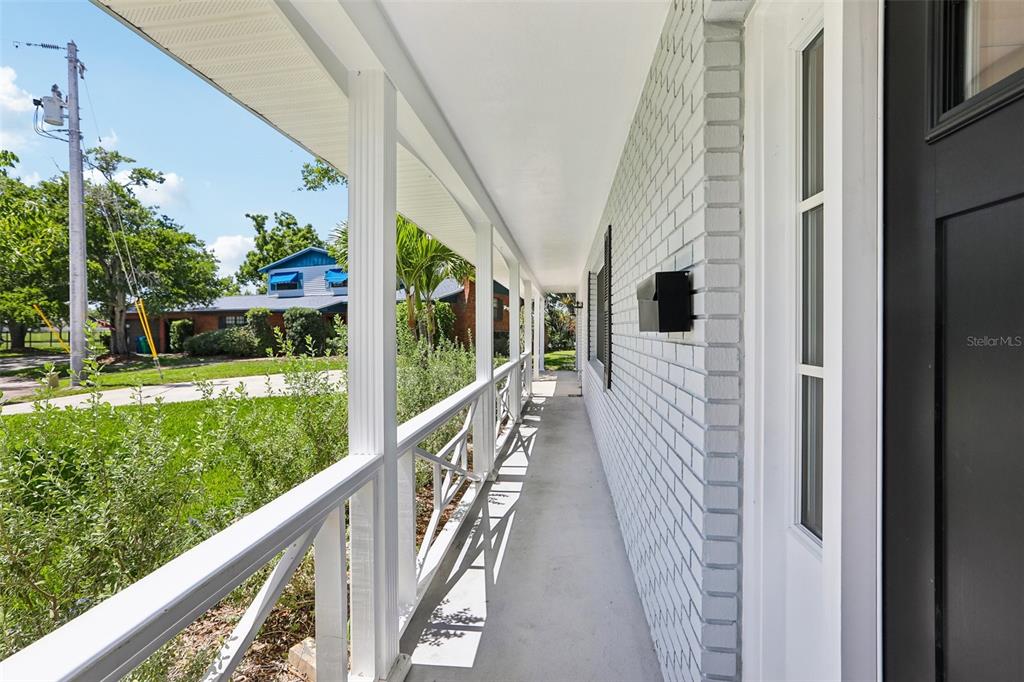 A covered porch with white railings and a painted brick wall leads to a front door — 6827 TEQUESTA DRIVE, SEMINOLE, FL