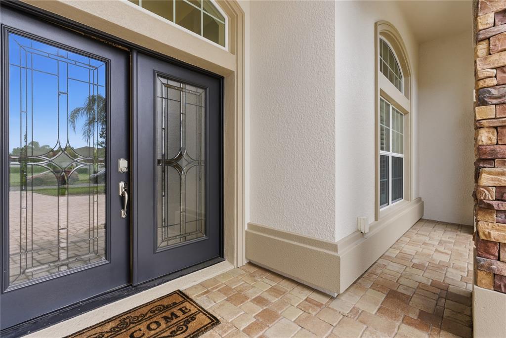 A dark double front door with glass inserts sits beside a window on a porch — 8747 BONICA PLACE, LAND O LAKES, FL