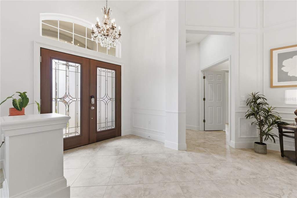 A bright foyer features a double wood door, tile flooring, and a crystal chandelier — 8747 BONICA PLACE, LAND O LAKES, FL