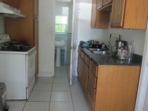 A galley kitchen features wood cabinets, a white stove, and a doorway leading to a bathroom — 402 N A Street, FL 33460, FL