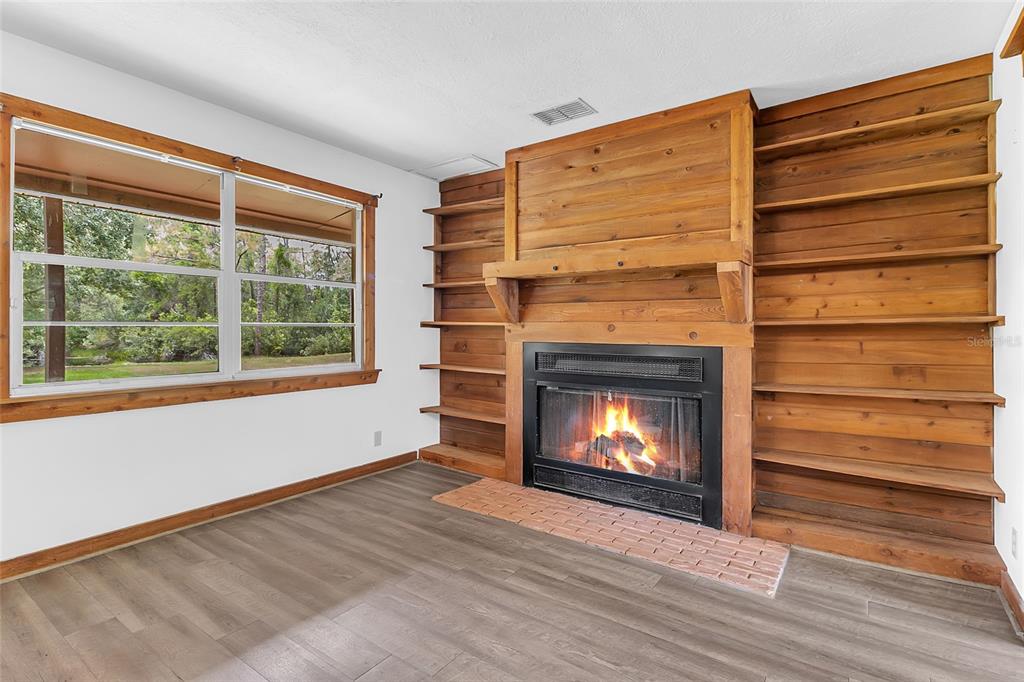 A living room features a wood-paneled fireplace, built-in shelving, wood-look flooring, and a large window — 4465 STORY ROAD, ST CLOUD, FL
