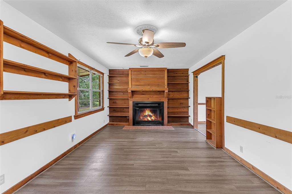 A living room features wood-paneled walls, built-in shelving, a fireplace, and light wood-look flooring — 4465 STORY ROAD, ST CLOUD, FL