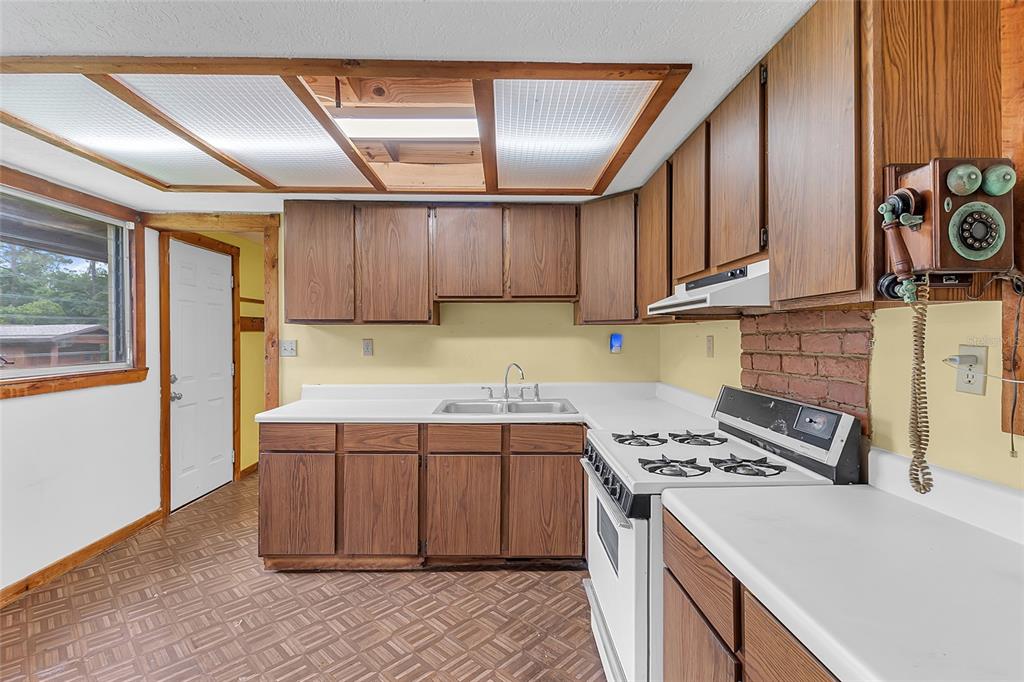 A kitchen features wood cabinets, white countertops, a gas stove, and a vintage wall-mounted telephone — 4465 STORY ROAD, ST CLOUD, FL