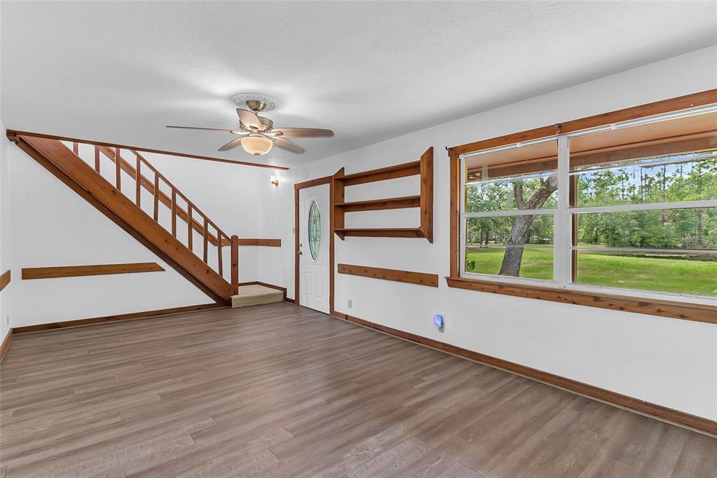 A living room with wood-look flooring, a wooden staircase, and a large window overlooking trees — 4465 STORY ROAD, ST CLOUD, FL