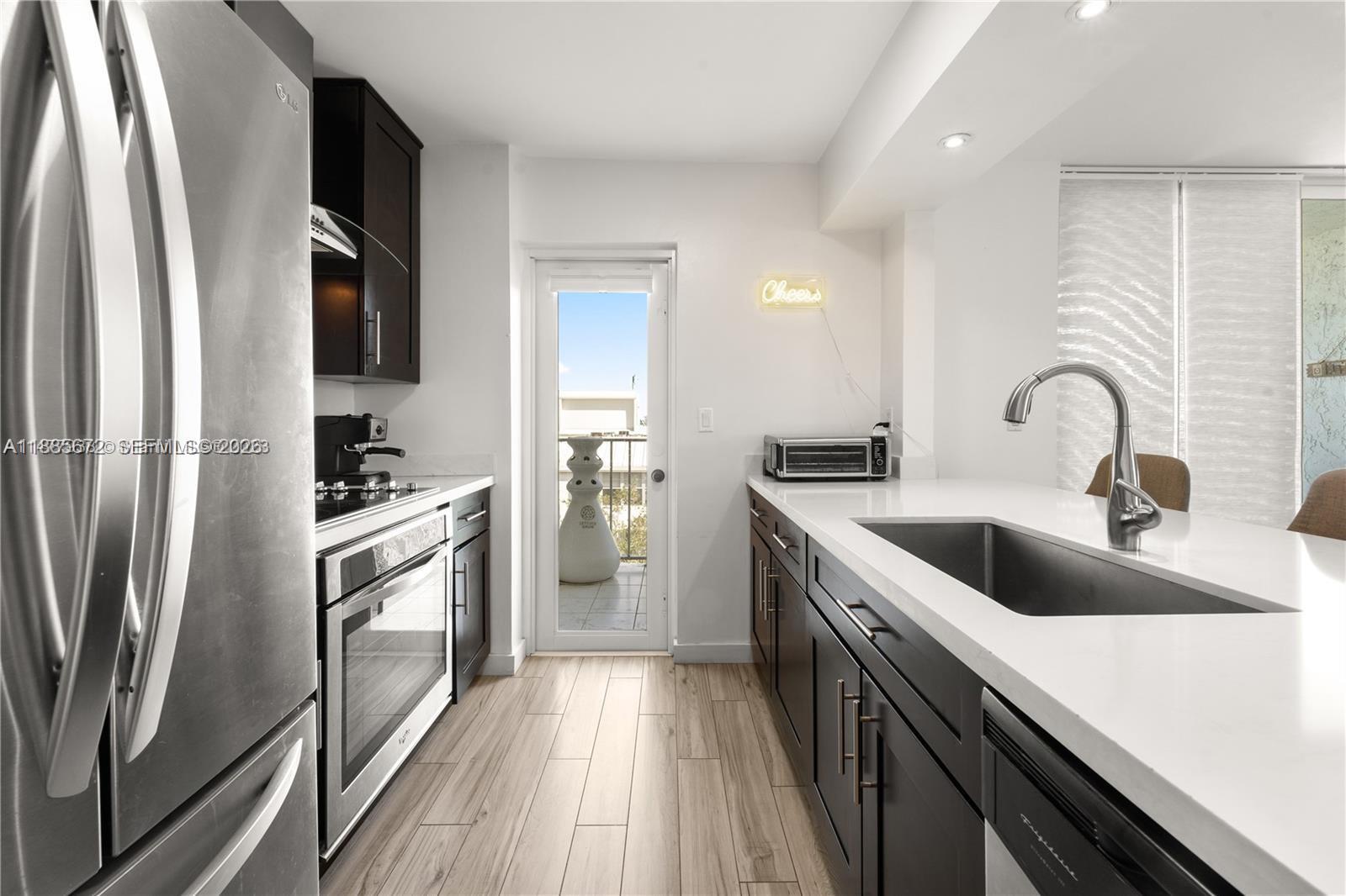 A modern kitchen features dark cabinetry, white countertops, stainless steel appliances, and a balcony door — 650 NE 64th St, Miami FL 33138, MIAMI, FL