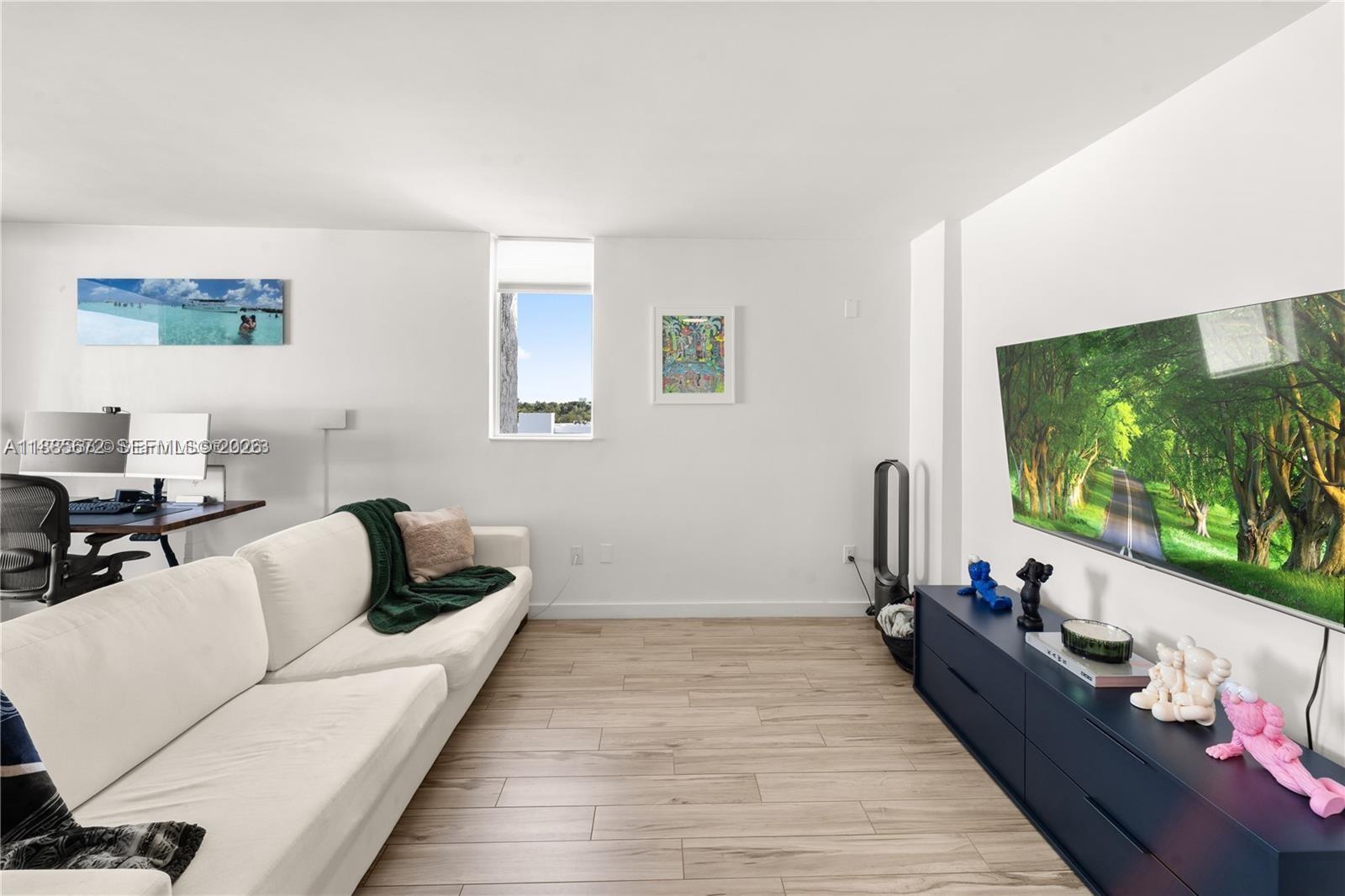 A living room features a white sofa, a dark blue media console, and light wood flooring — 650 NE 64th St, Miami FL 33138, MIAMI, FL
