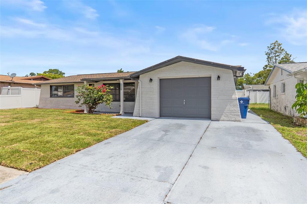 A single-story house with a white brick exterior, a gray garage door, and a concrete driveway — 6113 9TH AVENUE, NEW PORT RICHEY, FL