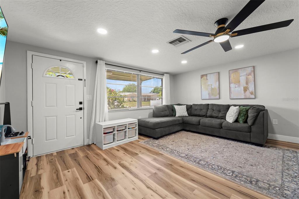 A living room features a gray sectional sofa, wood-look flooring, and a ceiling fan — 6113 9TH AVENUE, NEW PORT RICHEY, FL