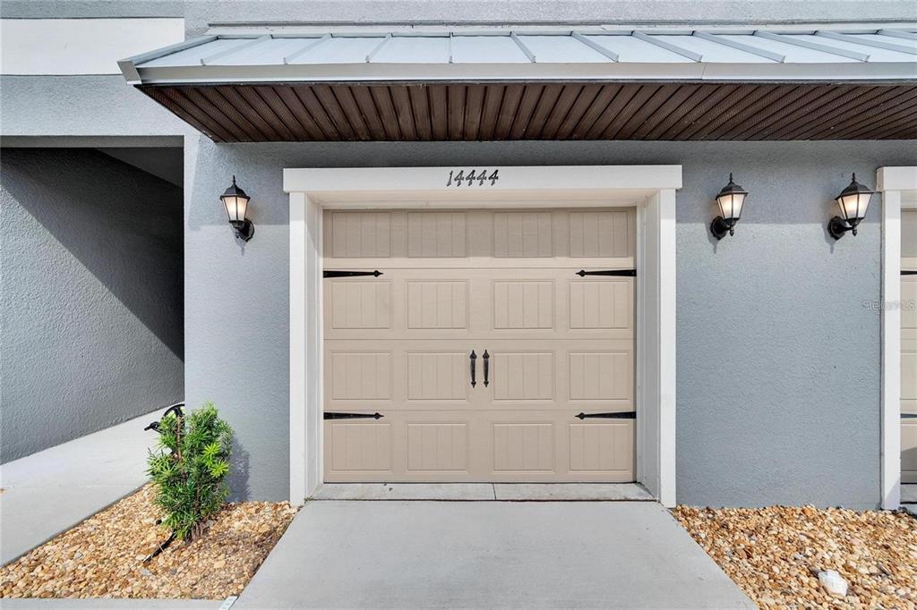 A beige garage door with black hardware is centered under a metal awning — 14444 EDITORS NOTE STREET, SUN CITY CENTER, FL