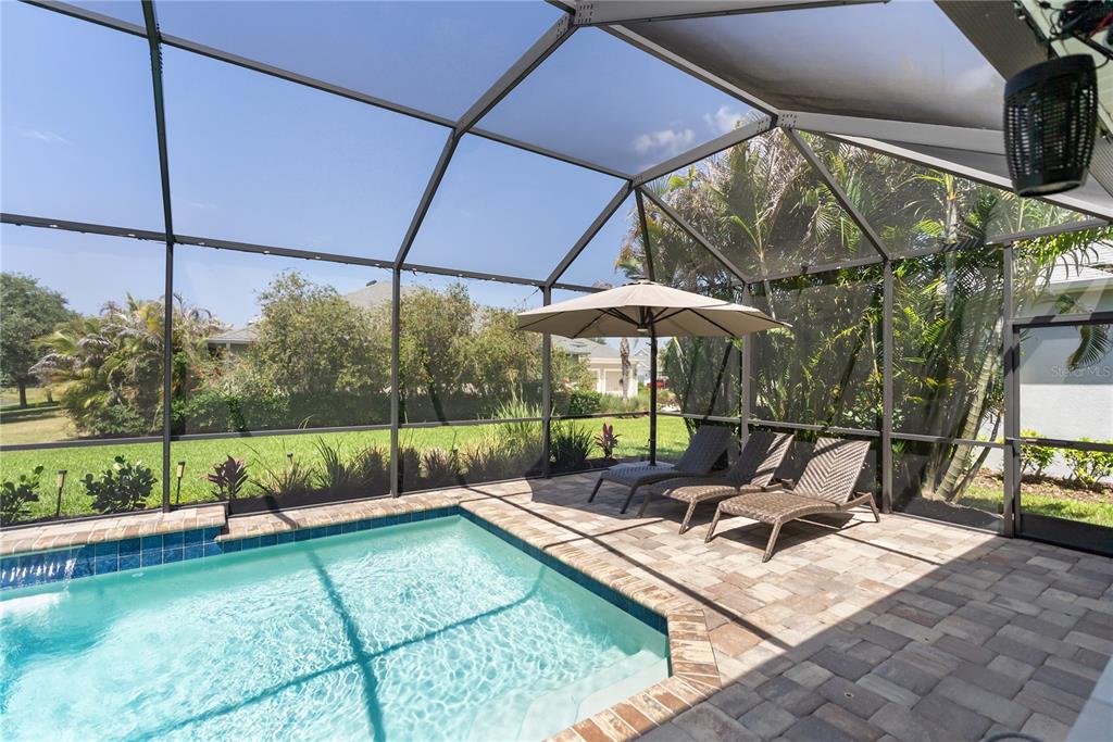 A covered patio features a dining set, a grill, and a screened-in pool overlooking water — 1215 THORNBURY DRIVE, PARRISH, FL