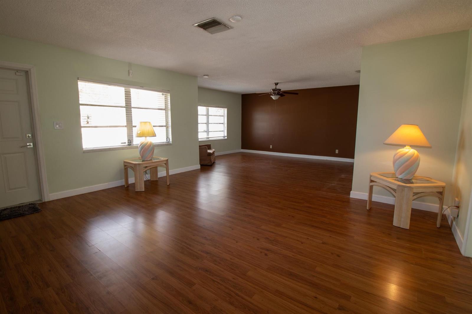 A spacious living room features light green walls, a dark brown accent wall, and wood flooring — 6860 Broadmoor, North Lauderdale FL 33068, NORTH LAUDERDALE, FL