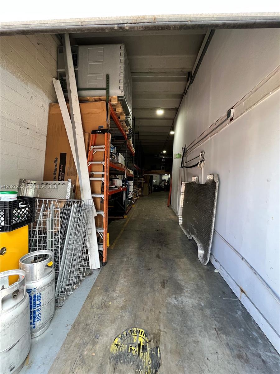A narrow storage area features concrete walls, metal shelving, and various equipment on a concrete floor — 8420 NW 61st St, Miami FL 33166, MIAMI, FL