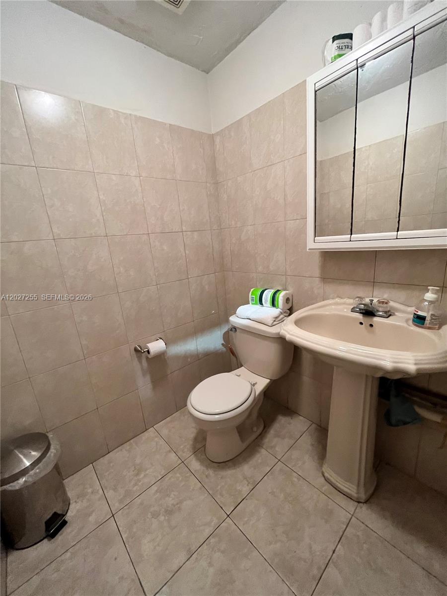 A small bathroom features beige tiled walls, a pedestal sink, and a white toilet — 8420 NW 61st St, Miami FL 33166, MIAMI, FL