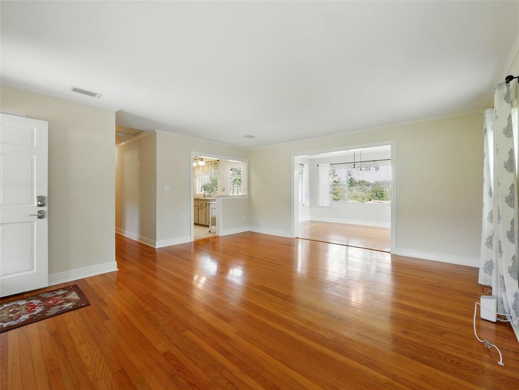 A living room with hardwood floors, a white door, and openings to a kitchen and sunroom — 1426 CRESTVIEW DRIVE, MOUNT DORA, FL