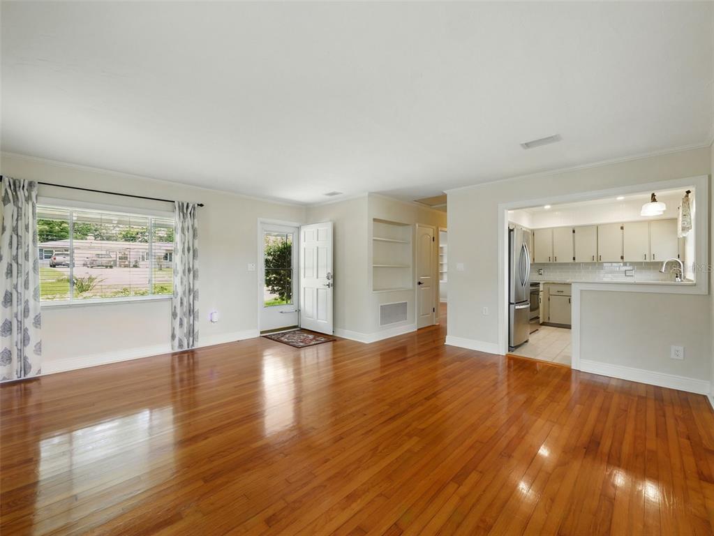 A living room with hardwood floors, a large window, and an open view into the kitchen — 1426 CRESTVIEW DRIVE, MOUNT DORA, FL