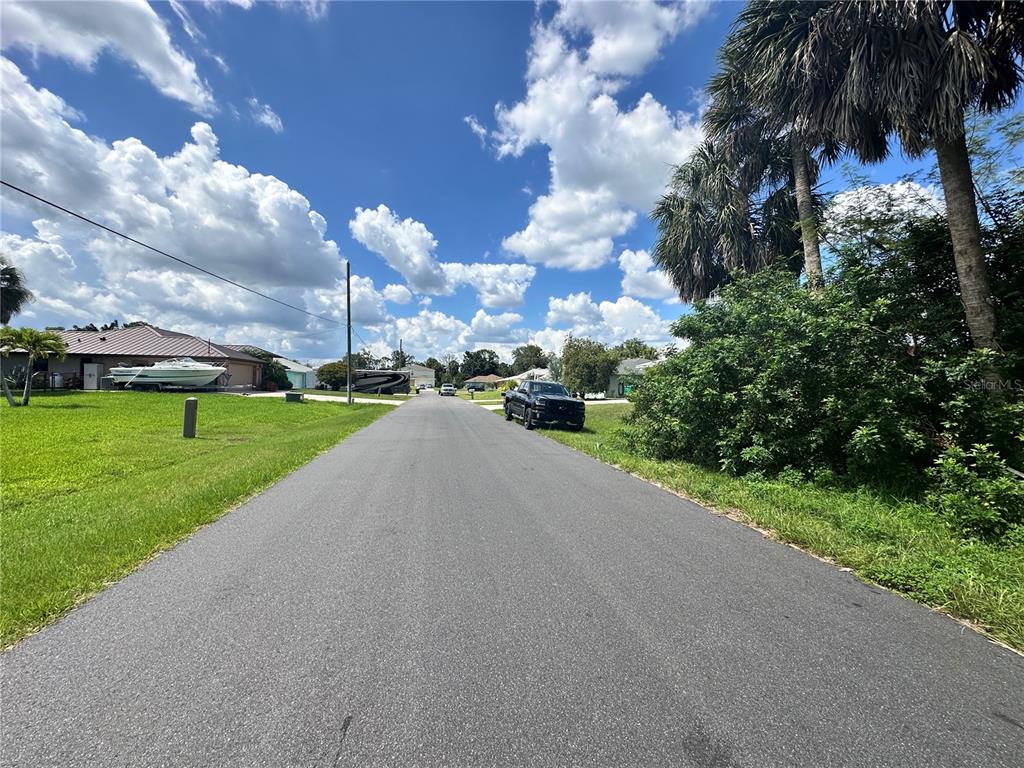 A paved residential street is lined with palm trees, green lawns, and a parked truck — 18394 GOODMAN CIRCLE, PORT CHARLOTTE, FL
