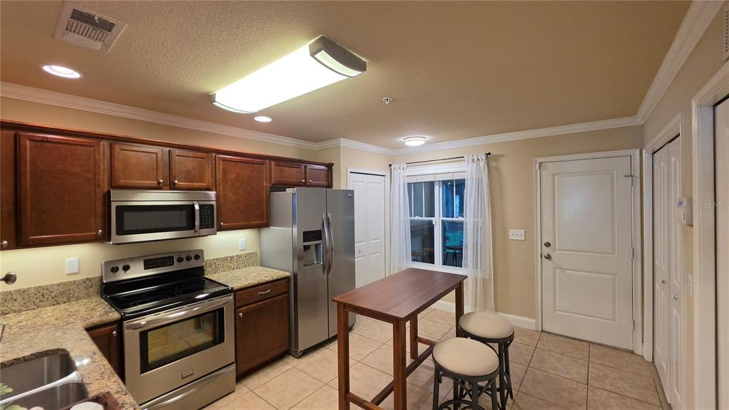A kitchen features wood cabinets, granite countertops, stainless steel appliances, and a small dining table — 4639 SW 48TH DRIVE UNIT 151, GAINESVILLE, FL