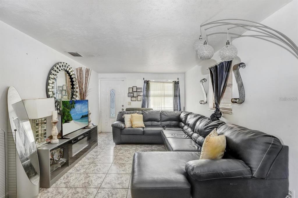 A living room features a large black sectional sofa, a television console, and tiled flooring — 4833 ASHLAND DRIVE, TAMPA, FL