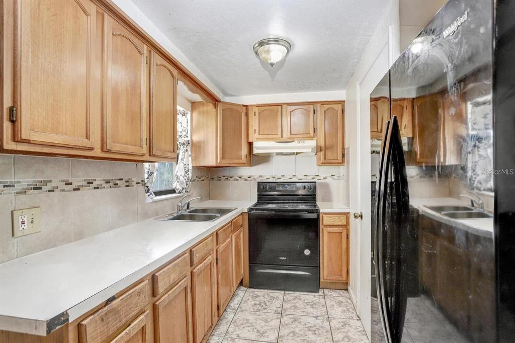 A galley kitchen features wood cabinets, white countertops, a black stove, and tiled flooring — 4833 ASHLAND DRIVE, TAMPA, FL