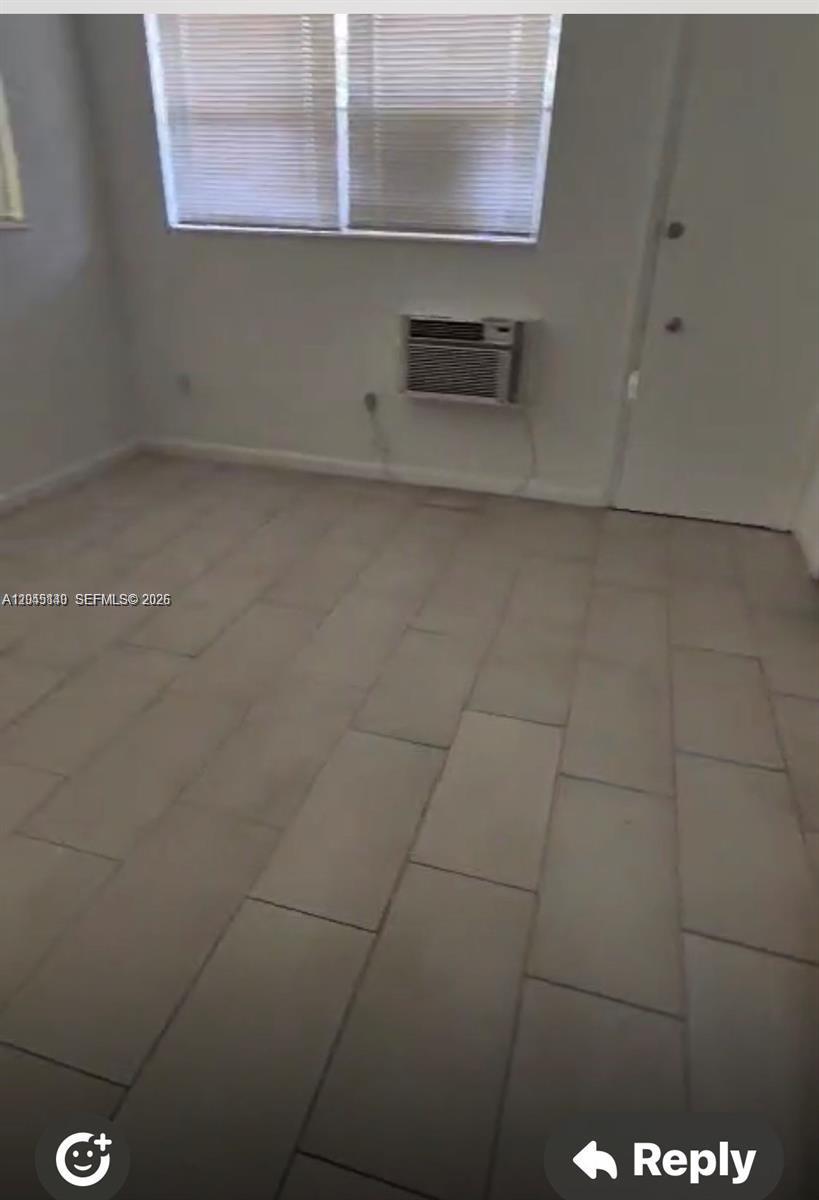 An empty room features light-colored tile flooring, a window with blinds, and a wall-mounted air conditioner — 285 NE 191st St # 2907, Miami FL 33179, MIAMI, FL