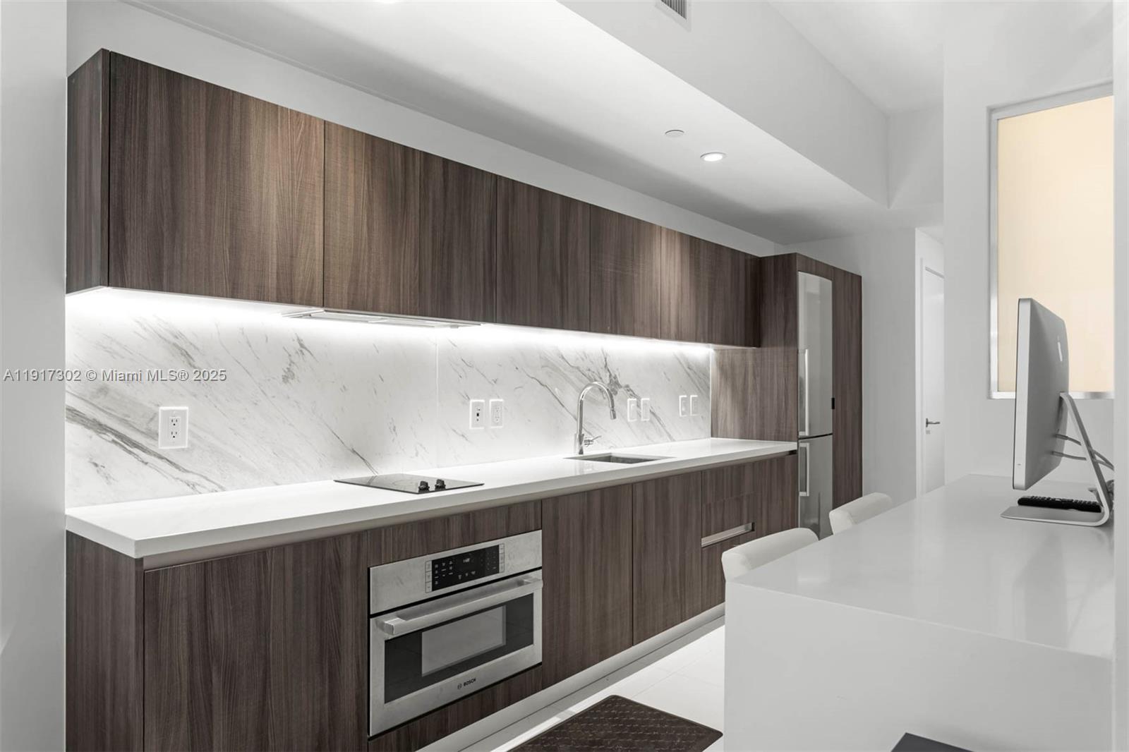 A modern kitchen features dark wood cabinetry, white countertops, and a marble backsplash — 851 NE 1st Ave # 300, Miami FL 33132, MIAMI, FL