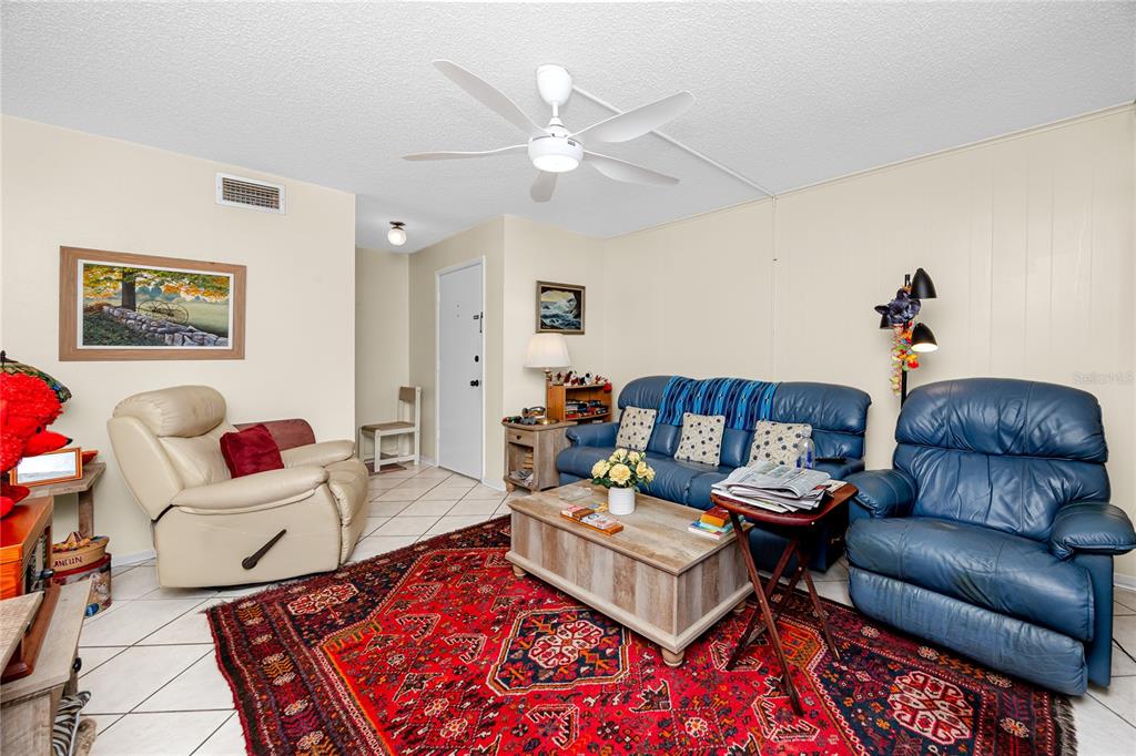 A living room features a red patterned rug, blue sofa, recliner, and ceiling fan — 3435 41ST TERRACE S UNIT 198, ST PETERSBURG, FL
