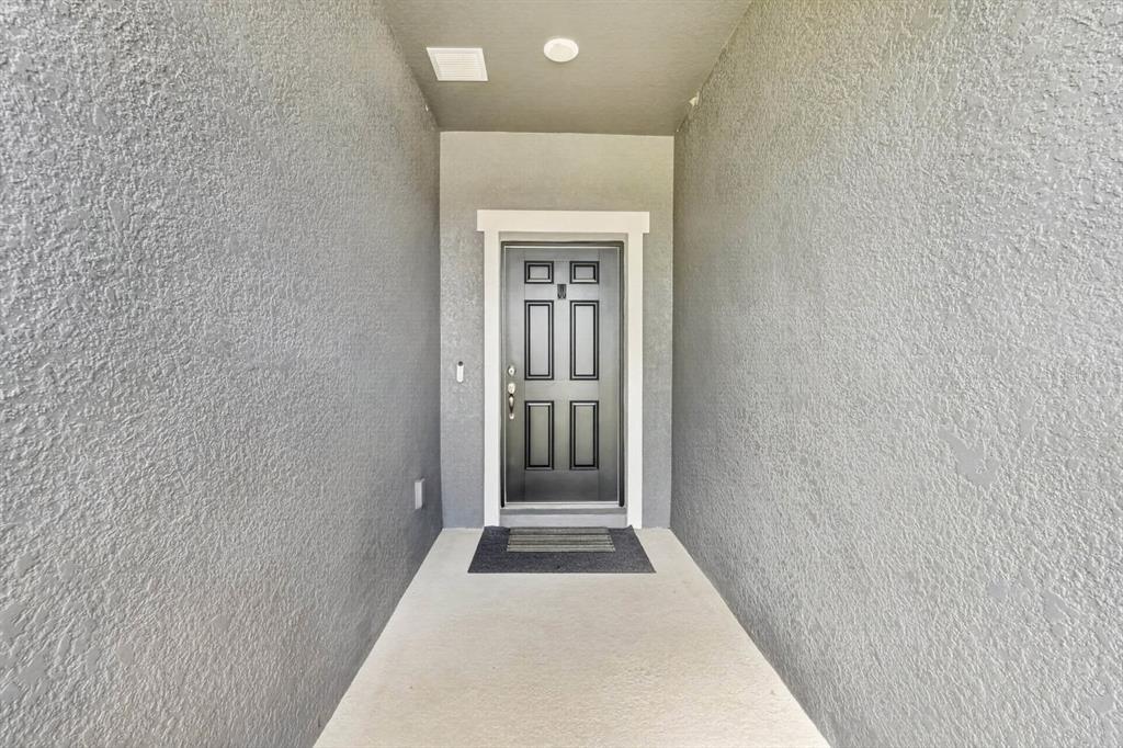 A gray front door with rectangular panels is set within a covered concrete entryway — 1615 MEADOWLARK DRIVE, DELTONA, FL