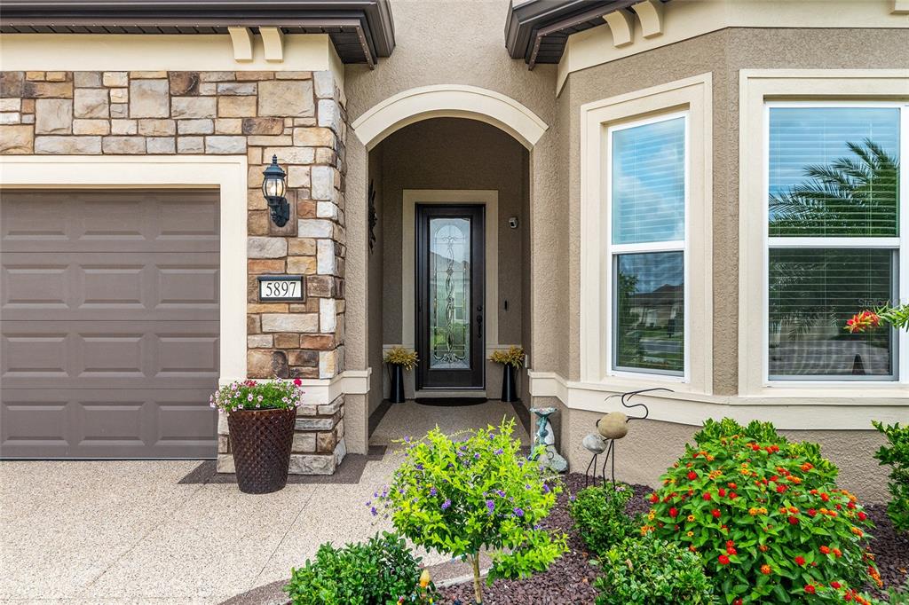 The exterior of a home features a stone-accented garage, arched entryway, and landscaped front garden — 5897 SW 90TH COURT ROAD, OCALA, FL