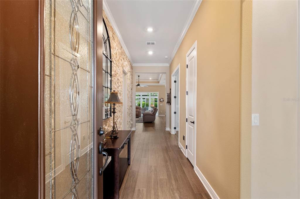 A foyer with wood-look tile flooring leads to a hallway featuring a stone accent wall — 5897 SW 90TH COURT ROAD, OCALA, FL