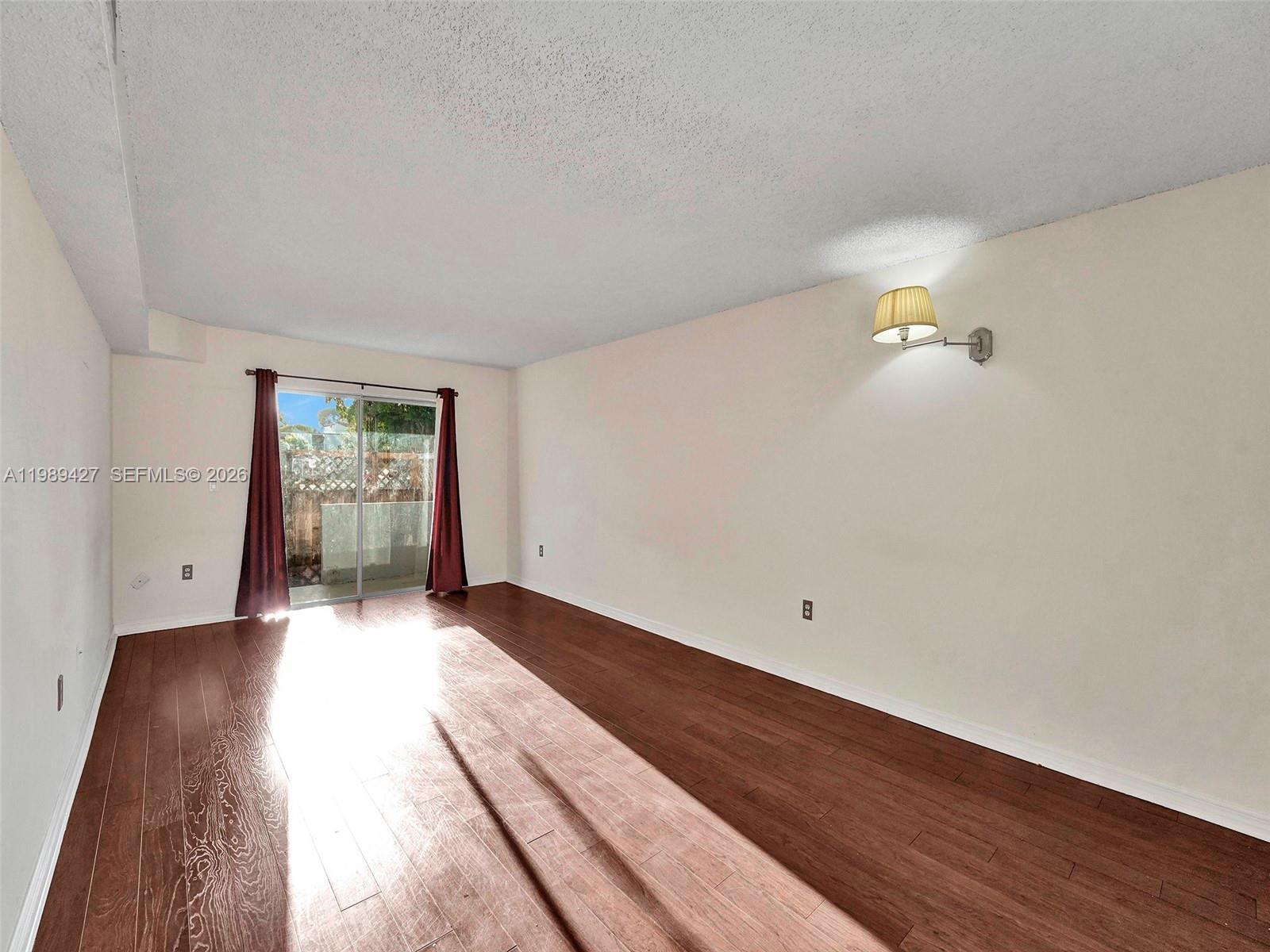 An empty room features dark wood flooring, white walls, a wall sconce, and sliding glass doors — 4600 SW 67th Ave # 155, Miami FL 33155, MIAMI, FL