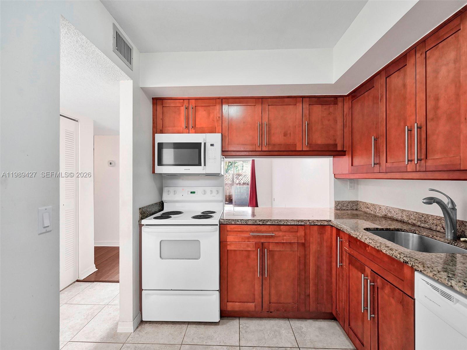 A kitchen features cherry wood cabinets, granite countertops, a white stove, and a stainless sink — 4600 SW 67th Ave # 155, Miami FL 33155, MIAMI, FL