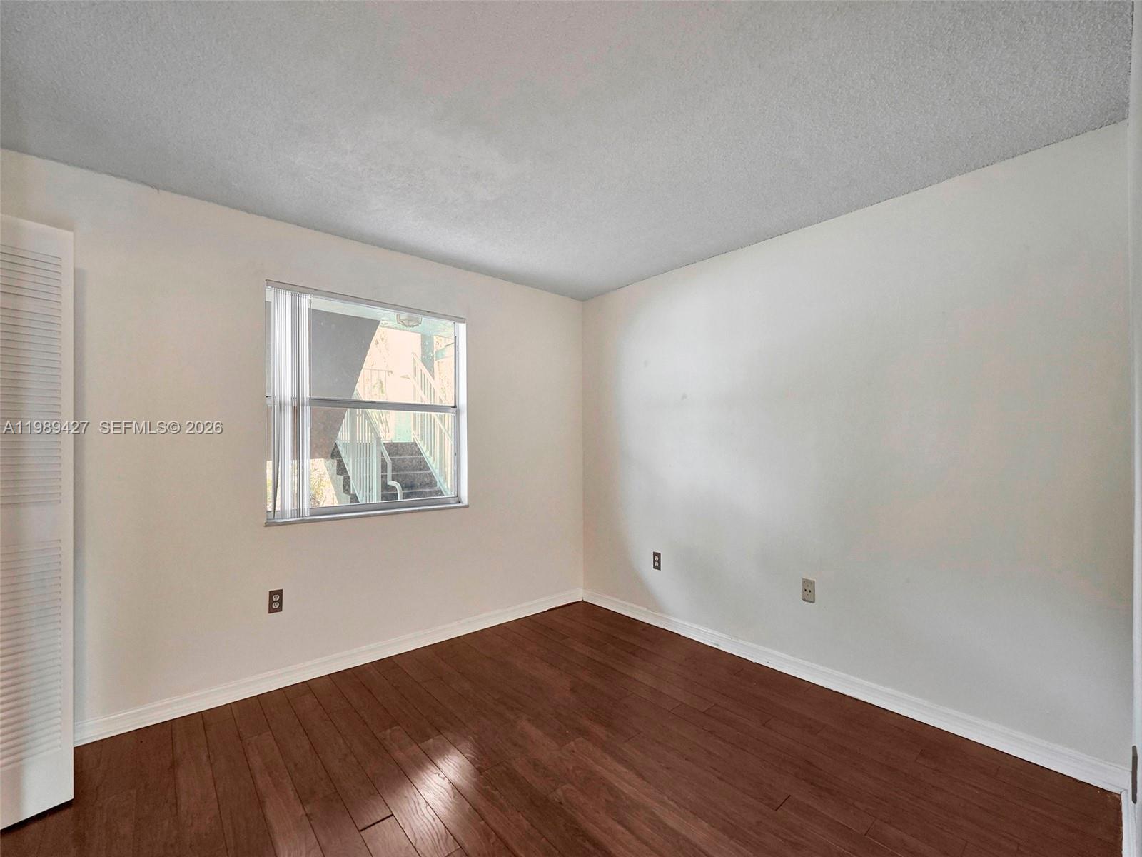 An empty bedroom features white walls, dark wood flooring, and a window overlooking exterior stairs — 4600 SW 67th Ave # 155, Miami FL 33155, MIAMI, FL