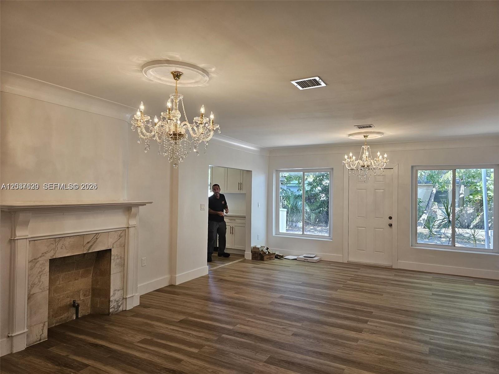A living room features a fireplace, two crystal chandeliers, and wood-look flooring — 1915 Normandy Dr, Miami Beach FL 33141, MIAMI BEACH, FL