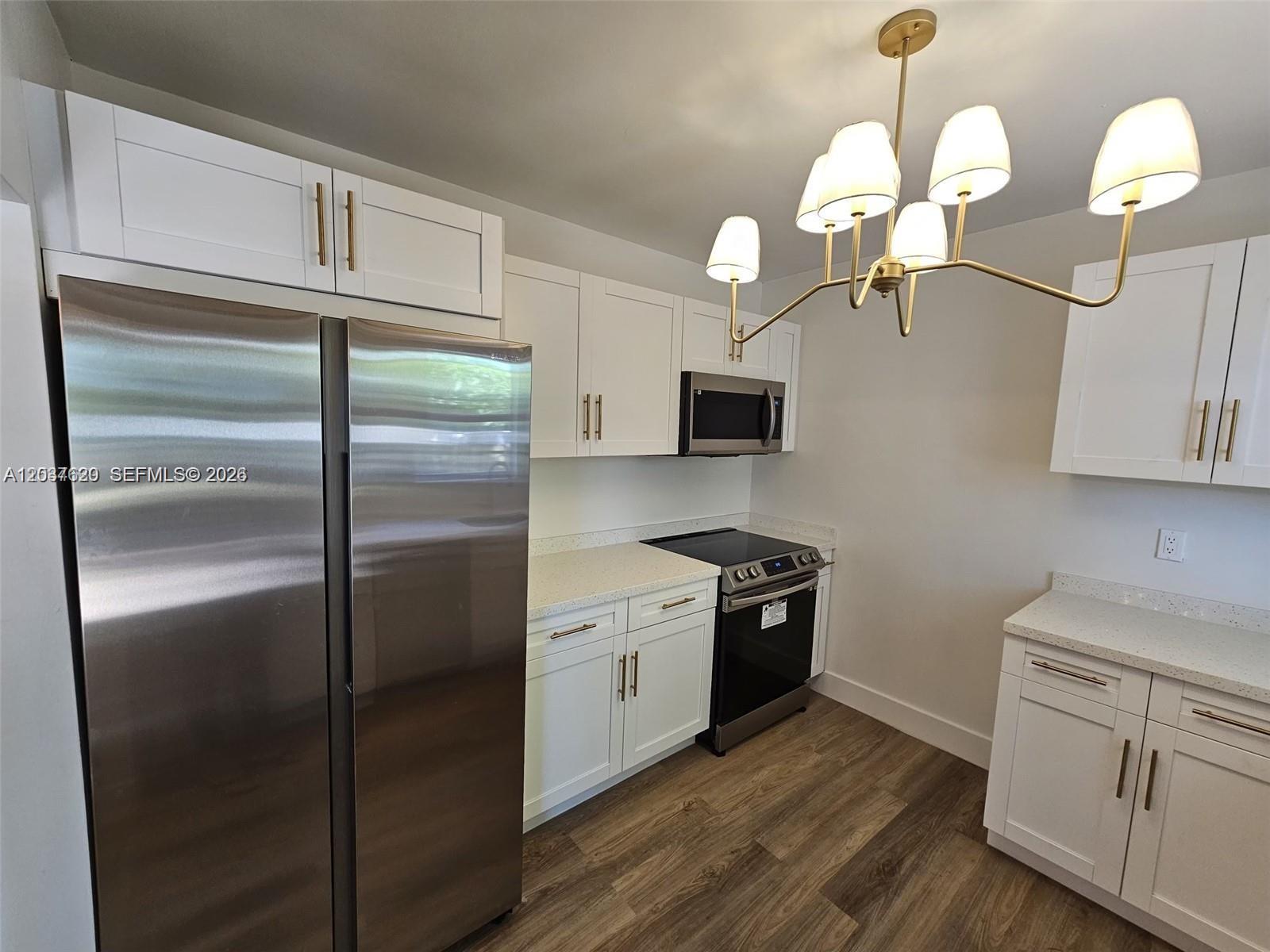 A kitchen features white cabinetry, stainless steel appliances, quartz countertops, and a modern chandelier — 1915 Normandy Dr, Miami Beach FL 33141, MIAMI BEACH, FL