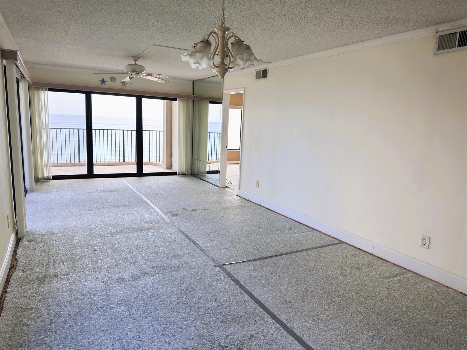 An empty room with a textured ceiling, chandelier, mirrored wall, and sliding doors overlooking the ocean — 10310 S Ocean Drive # 301, Jensen Beach FL 34957, JENSEN BEACH, FL
