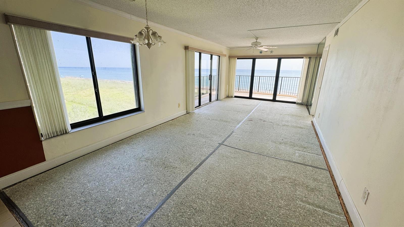 An empty room with carpeted floors, large windows, and sliding doors overlooking the ocean — 10310 S Ocean Drive # 301, Jensen Beach FL 34957, JENSEN BEACH, FL