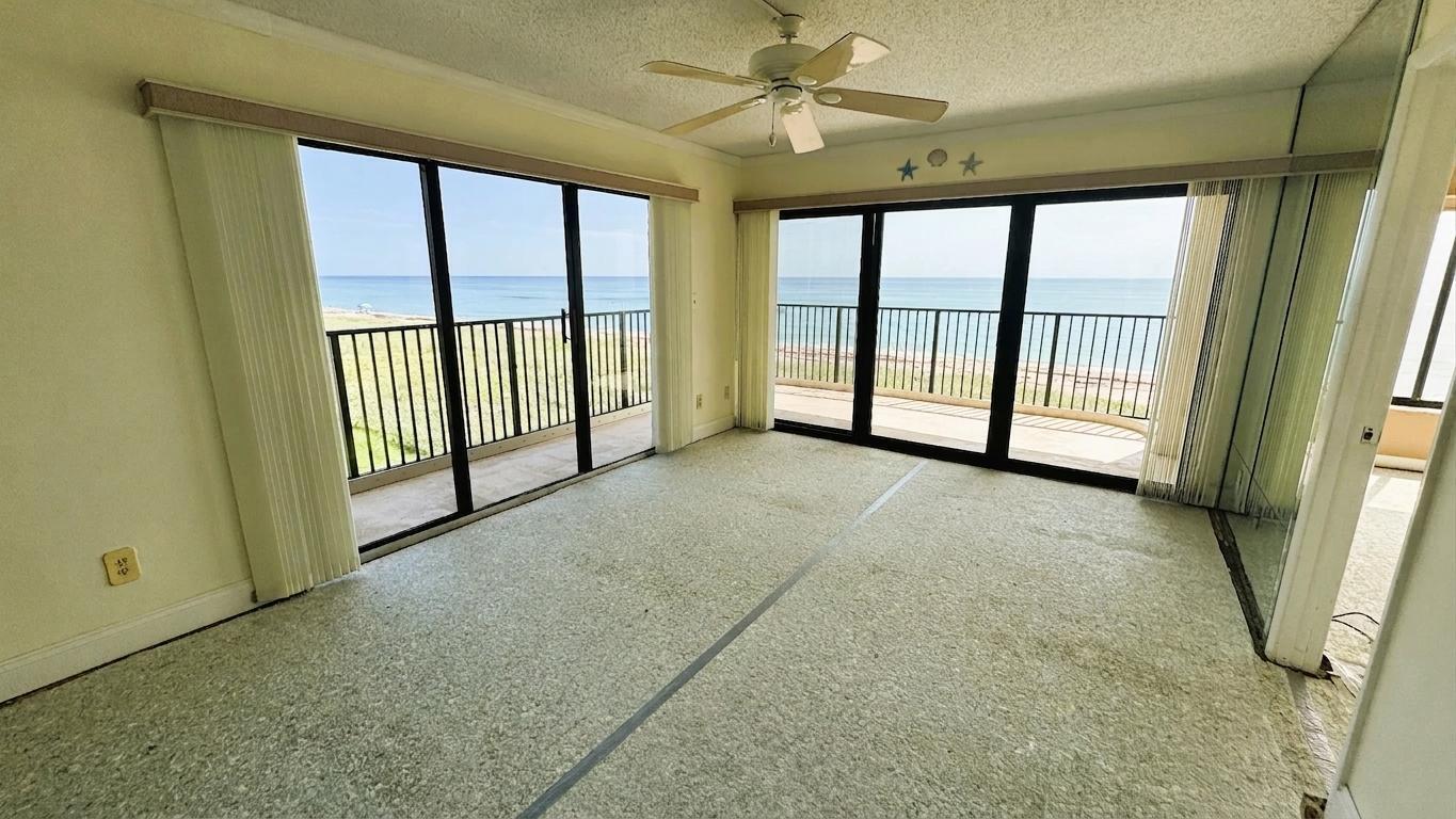 An empty room features beige carpet, a ceiling fan, and sliding glass doors overlooking the ocean — 10310 S Ocean Drive # 301, Jensen Beach FL 34957, JENSEN BEACH, FL