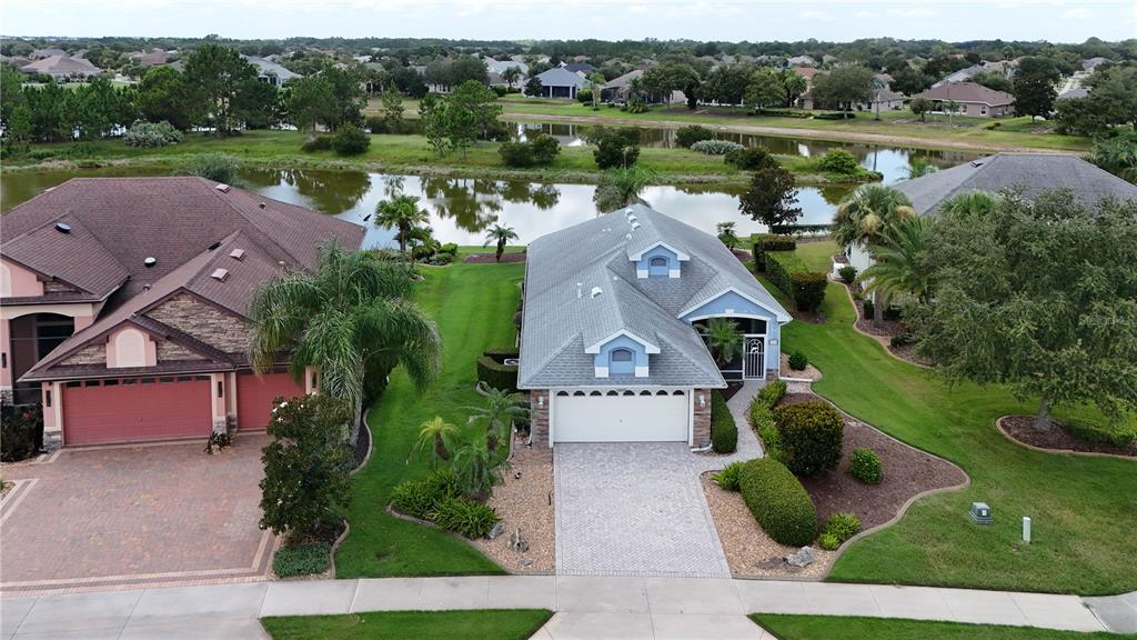 An aerial view shows two suburban houses with paved driveways, green lawns, and a pond — 2416 BAR HARBOR, MOUNT DORA, FL