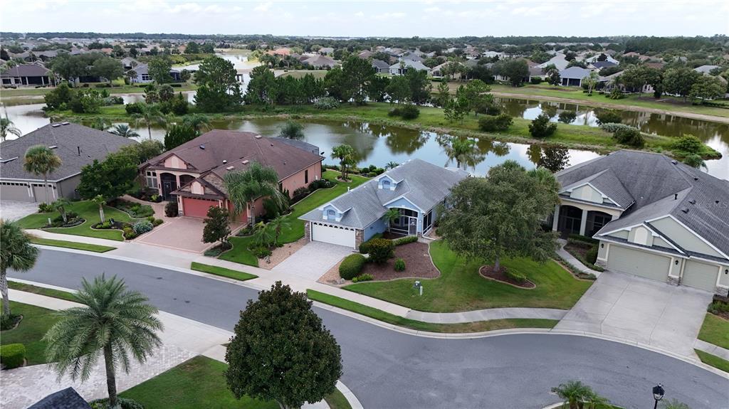 An aerial view shows three suburban houses with driveways and lawns bordering a small lake — 2416 BAR HARBOR, MOUNT DORA, FL