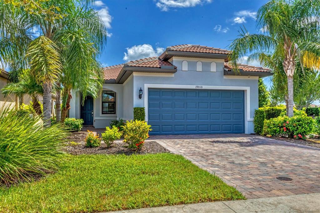 A single-story house with a blue garage door, tile roof, and palm trees in the yard — 19010 MANGIERI STREET, VENICE, FL