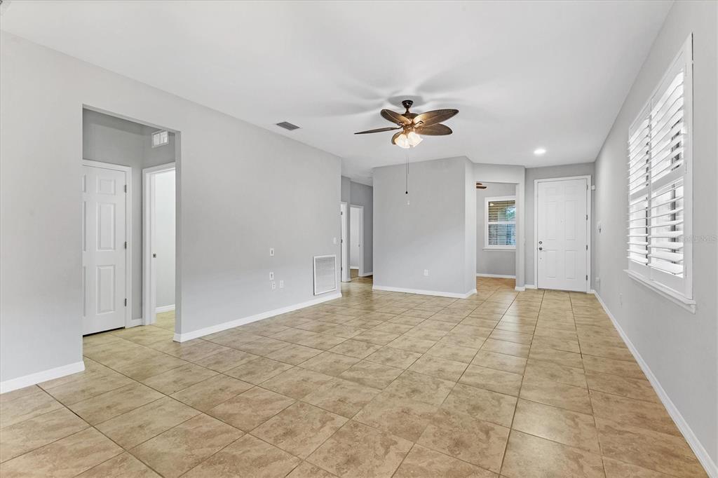 An empty living room features light gray walls, tan tile flooring, and a ceiling fan — 19010 MANGIERI STREET, VENICE, FL