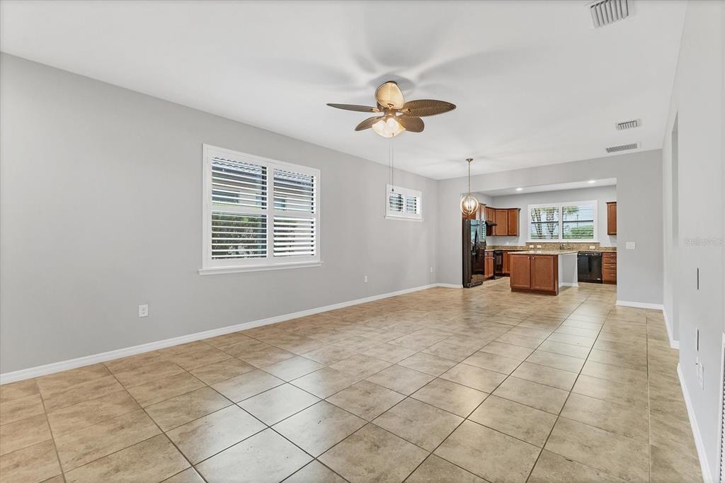A spacious room with light gray walls, tile flooring, a ceiling fan, and an open kitchen — 19010 MANGIERI STREET, VENICE, FL