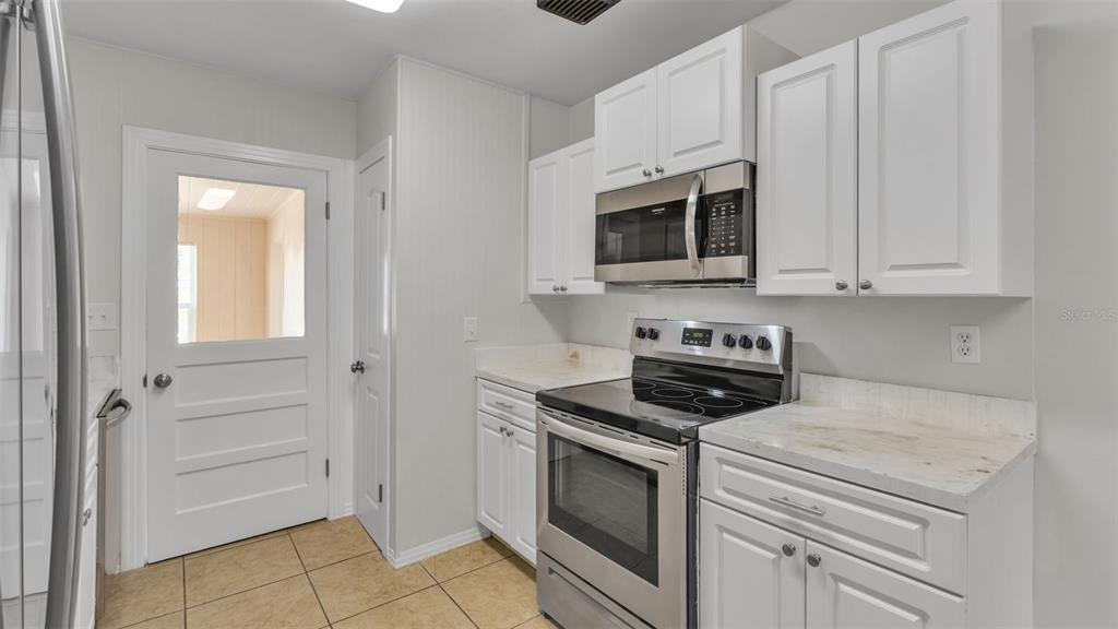 A kitchen features white cabinets, stainless steel appliances, and light-colored countertops over tile flooring — 614 W SHADY LANE, LAKELAND, FL