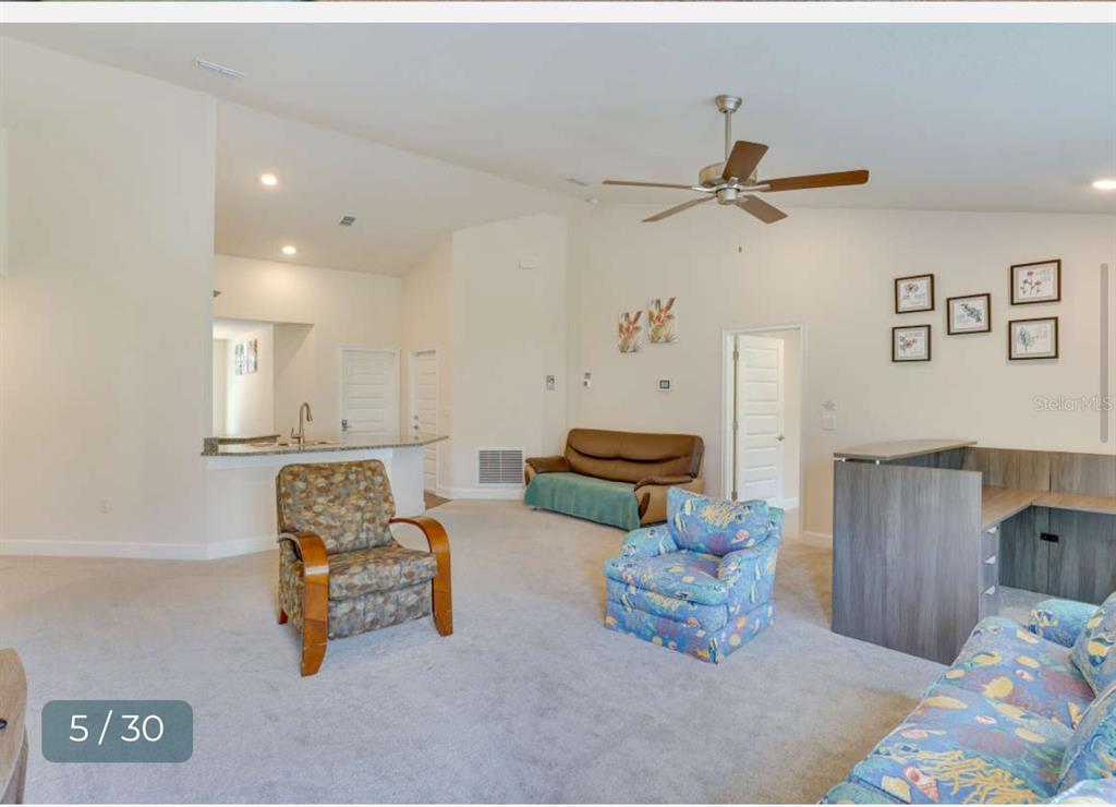 A living room with carpeted floors, a ceiling fan, and a kitchen counter in view — 303 SHAD WAY, POINCIANA, FL