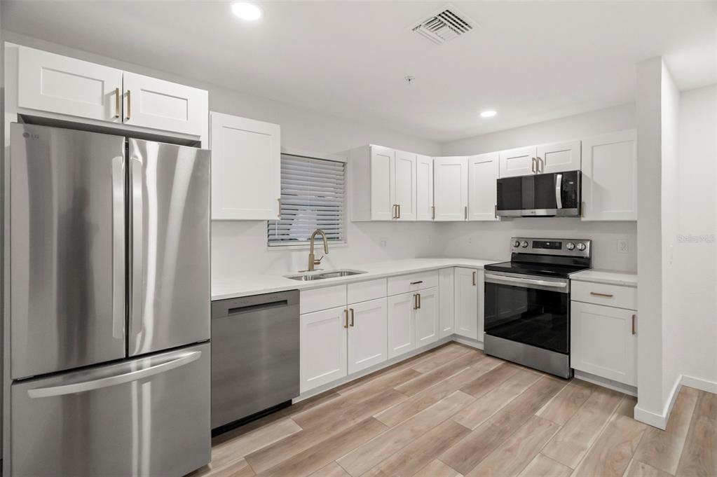 A kitchen features white cabinets, stainless steel appliances, and light wood-look flooring — 3103 16TH STREET N, ST PETERSBURG, FL